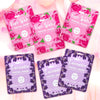 Image of 6 packs of facial masks on a pink background. 3 of the packs are in pink for the rose water masks, 3 of the packs are in purple for the lavender masks.